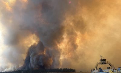 Smoke and flames rise from a wildfire near a body of water, with a boat in the foreground, il — wildfires impact on tribes
