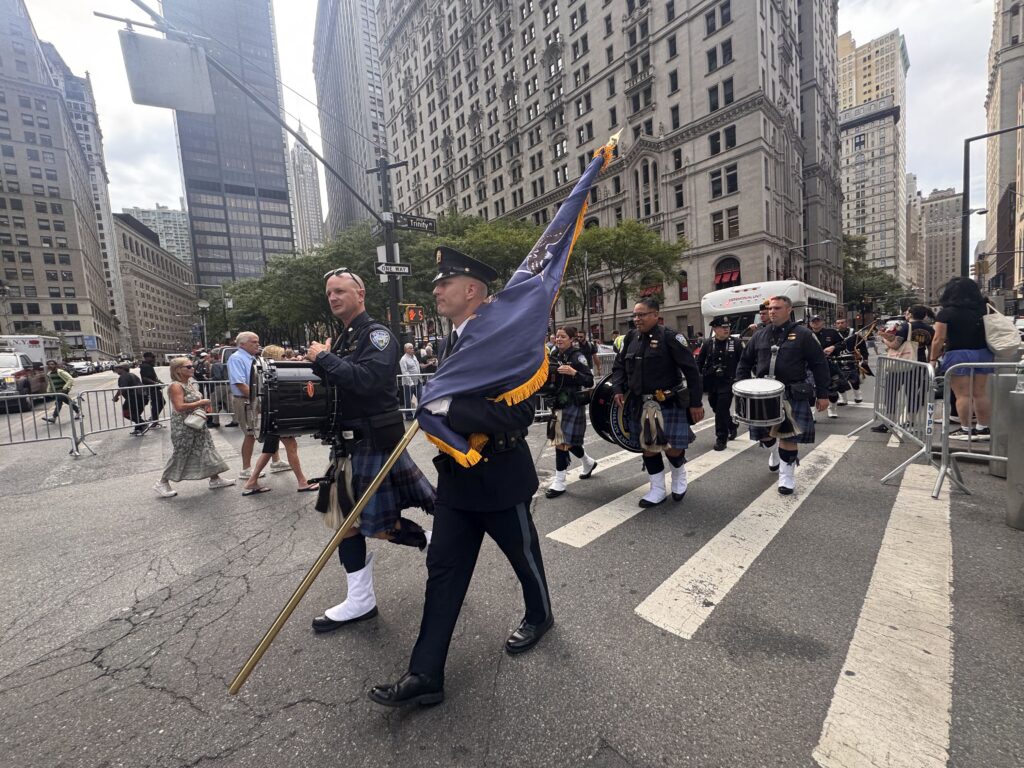 A procession of bagpipers and drummers in uniform marching down a city street, honor — 25th anniversary of Sept 11 attacks
