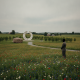 A person stands in a meadow of wildflowers near a memorial boulder and a circular monument. — Flight 93 25th anniversary