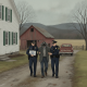 Two police officers escort a man in handcuffs along a rural road near a farmhouse and barn in P — Pownal VT Forgery Arrest