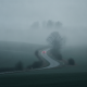 A winding road through a foggy landscape with a red car visible in the distance, illustratin — dense fog Bennington County