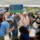 A diverse group of people gather under a tent, discussing tax initiatives and signing petition — state tax ballot measures