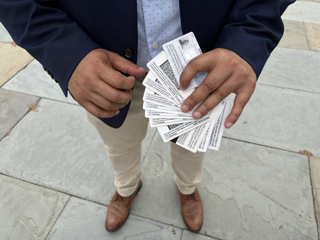 A person holding multiple identification cards in their hands, standing on a stone surface. — TPS El Salvador Expiration