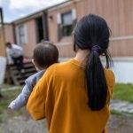 A woman holding a baby walks towards a mobile home, highlighting concerns over the new public charge rule.