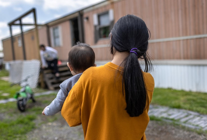 A woman holding a baby walks towards a mobile home, highlighting concerns over the new public charge rule.