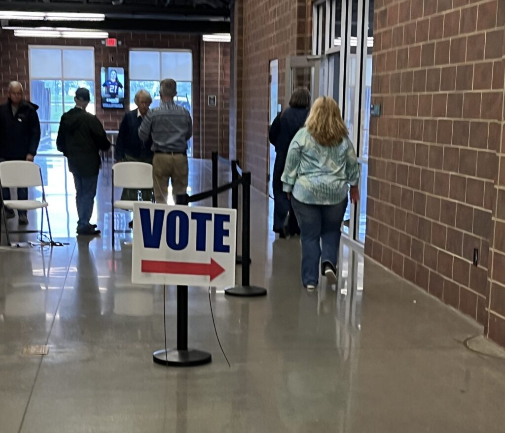 Voters entering a polling place with a 'Vote' sign pointing the way during election season. — ICE at polling places lawsuit