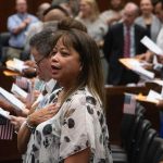 A woman places her hand over her heart as people hold small U.S. flags during — Trump administration naturalization delays