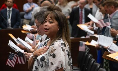 A woman places her hand over her heart as people hold small U.S. flags during — Trump administration naturalization delays