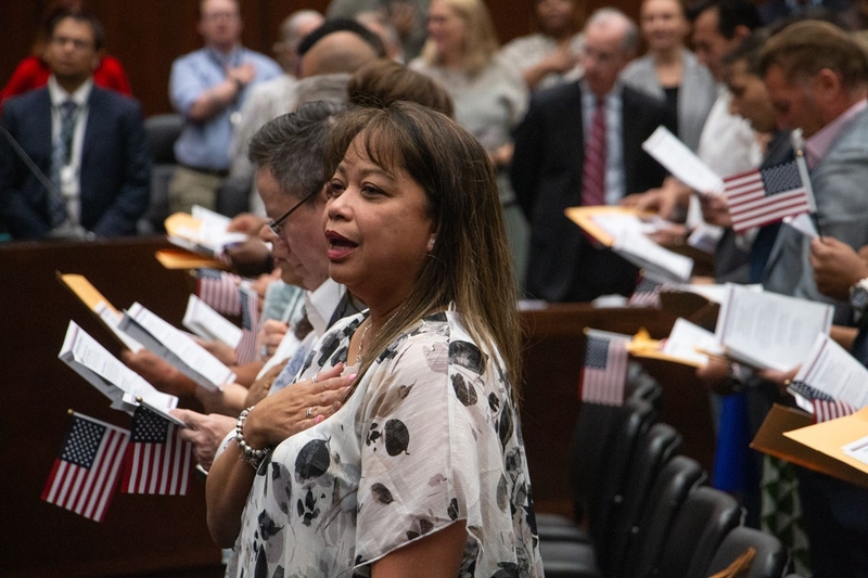 A woman places her hand over her heart as people hold small U.S. flags during — Trump administration naturalization delays