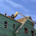 Construction worker on a roof of a building with green sheathing under a blue sky, — Massachusetts housing ballot measure