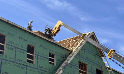Construction worker on a roof of a building with green sheathing under a blue sky, — Massachusetts housing ballot measure