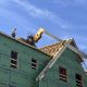 Construction worker on a roof of a building with green sheathing under a blue sky, — Massachusetts housing ballot measure