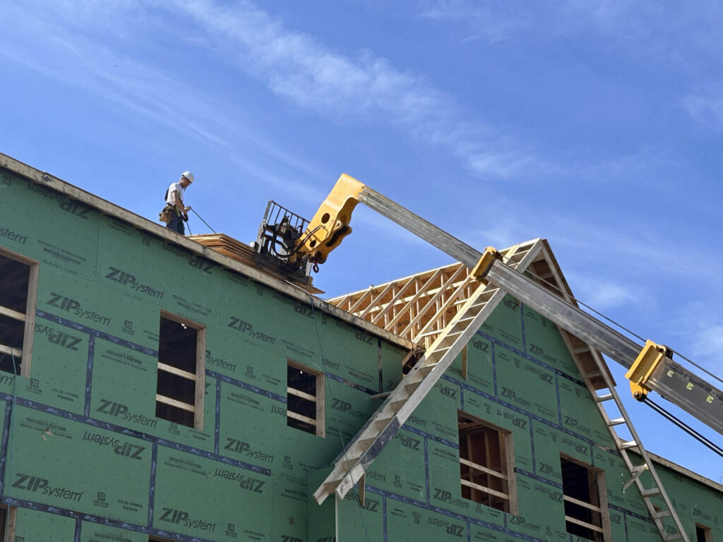 Construction worker on a roof of a building with green sheathing under a blue sky, — Massachusetts housing ballot measure