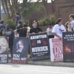 Criminal charges during pregnancy debate reflected in a sidewalk protest, with people holding anti-abortion signs and feta…