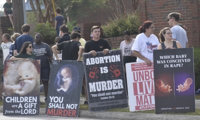 Criminal charges during pregnancy debate reflected in a sidewalk protest, with people holding anti-abortion signs and feta…