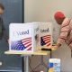 Two people use private voting booths decorated with “I Voted” signs and American f — noncitizen voting ballot measures