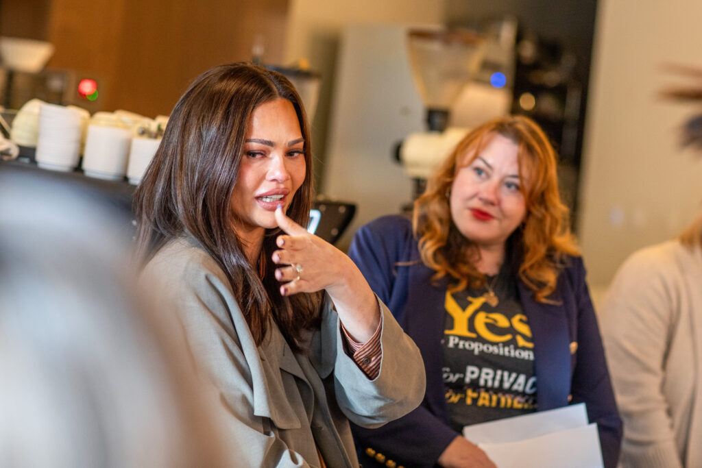 Chrissy Teigen Idaho abortion advocacy: Teigen speaks beside a woman wearing a “Yes” campaign shirt.