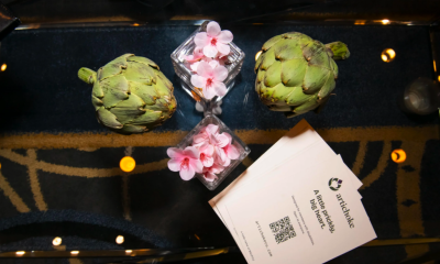 Artichokes, pink blossoms, and an Artichoke Credit Union business card arranged on a reflective table