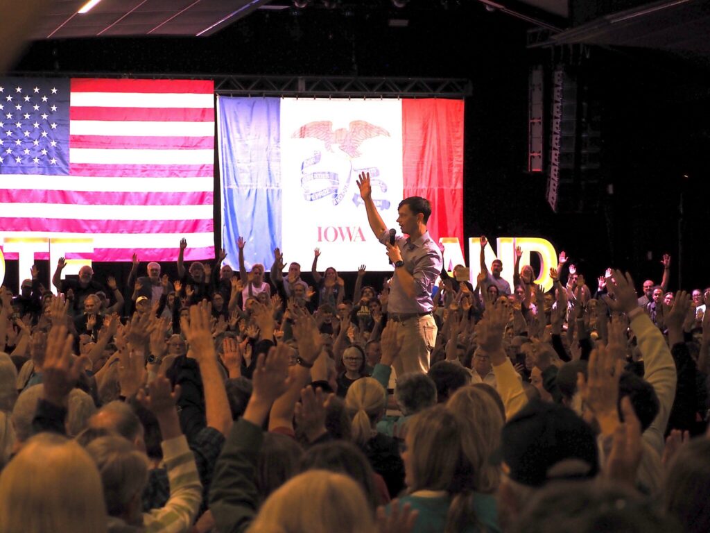 A crowd raises their hands in response to a speaker at a political rally with Am — Democrats majority of governors offices