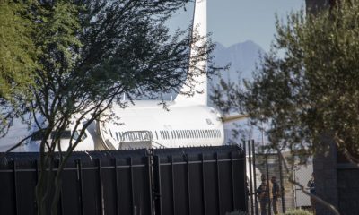 Trump deportation analysis: a white passenger plane behind a tall black fence, with people nearby
