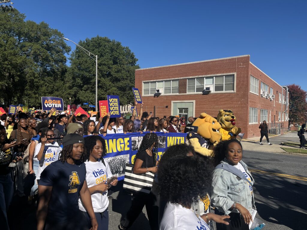 College Student Voting Access rally with students carrying voter signs and university mascots marching along a campus street