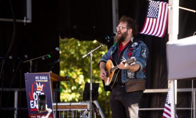 Musician performing at a No Kings movement rally with a guitar and an American flag in th — No Kings movement early voting