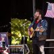 Musician performing at a No Kings movement rally with a guitar and an American flag in th — No Kings movement early voting