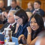 A diverse group of lawmakers in a legislative chamber, with a focus on a young woman smiling at the ca — Gen Z politicians