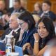 A diverse group of lawmakers in a legislative chamber, with a focus on a young woman smiling at the ca — Gen Z politicians