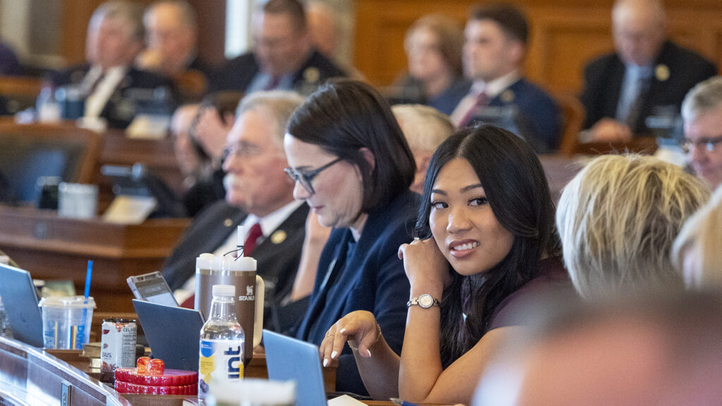 A diverse group of lawmakers in a legislative chamber, with a focus on a young woman smiling at the ca — Gen Z politicians