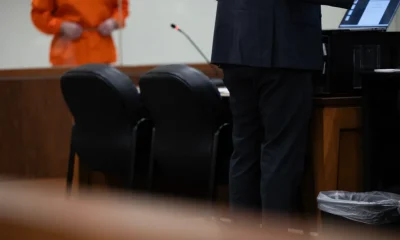 A public defender stands at a courtroom table while a client in an orange jumpsuit waits in the — public defender shortage