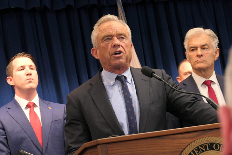 Robert F. Kennedy Jr. speaking at a podium with two men in suits behind him, in a formal — FDA abortion pill safety review