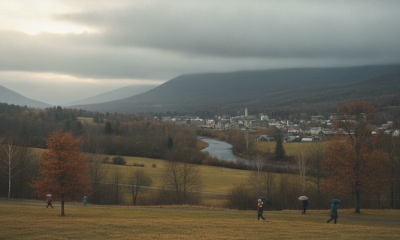 Bennington VT weather forecast: people walk across a grassy field beneath overcast skies, with autumn hills and a river be…