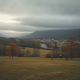 Bennington VT weather forecast: people walk across a grassy field beneath overcast skies, with autumn hills and a river be…