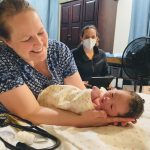 A woman cradles a newborn beside a masked caregiver; Vermont birth centers are the story context.
