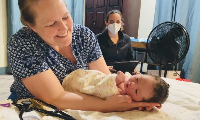 A woman cradles a newborn beside a masked caregiver; Vermont birth centers are the story context.