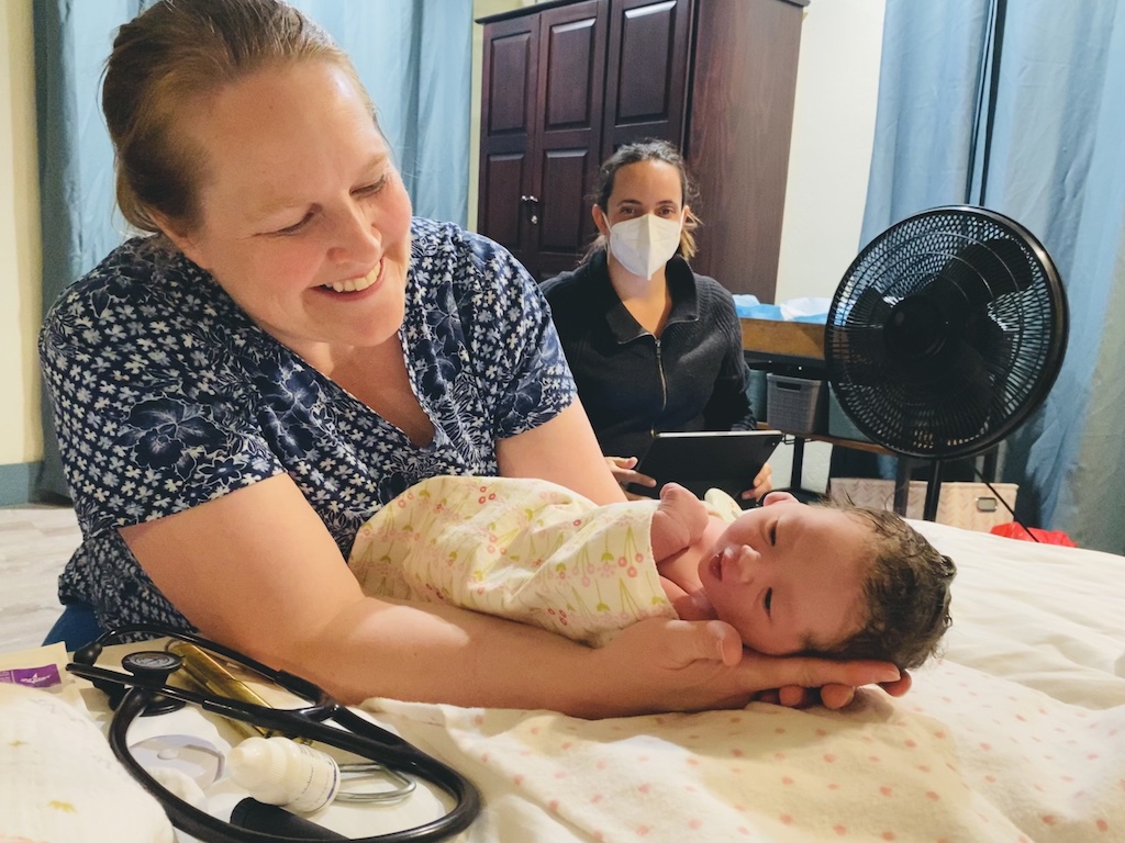 A woman cradles a newborn beside a masked caregiver; Vermont birth centers are the story context.