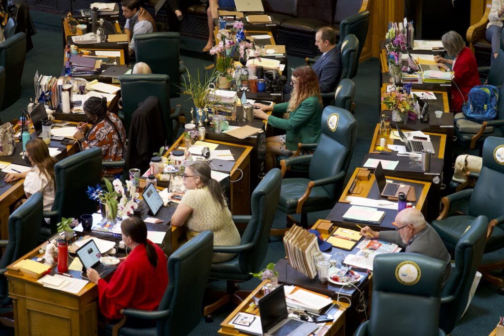 Women running for state legislature are reflected in an overhead view of lawmakers working at desks in a chamber.