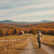 A person stands on a country lane overlooking an autumn valley beneath a cloudy sk — Bennington County VT weather forecast