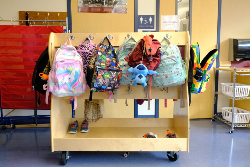 Colorful backpacks hanging on a wooden rack in a school hallway, with shoes underne — Education Freedom Tax Credit program