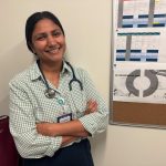 A smiling female doctor with a stethoscope stands with arms crossed in front of a bul — foreign doctors physician shortage