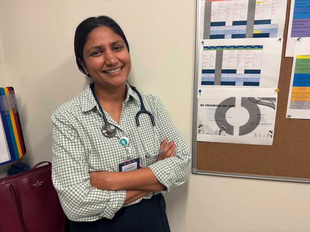 A smiling female doctor with a stethoscope stands with arms crossed in front of a bul — foreign doctors physician shortage