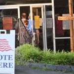 DOJ election monitors 2026 story: voters enter a polling place beside a “Vote Here” sign.