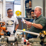 Workers gather around machinery in a workshop, illustrating the labor challenges affecting new home completions.