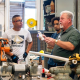 Workers gather around machinery in a workshop, illustrating the labor challenges affecting new home completions.