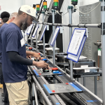Workers operate equipment along an industrial production line, illustrating Vermont Job Losses and employment trends.