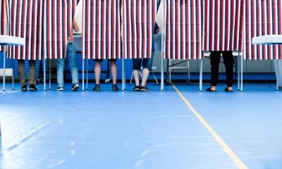 Voters standing behind striped privacy curtains in a polling place during an election. — Trump voter roll data lawsuit