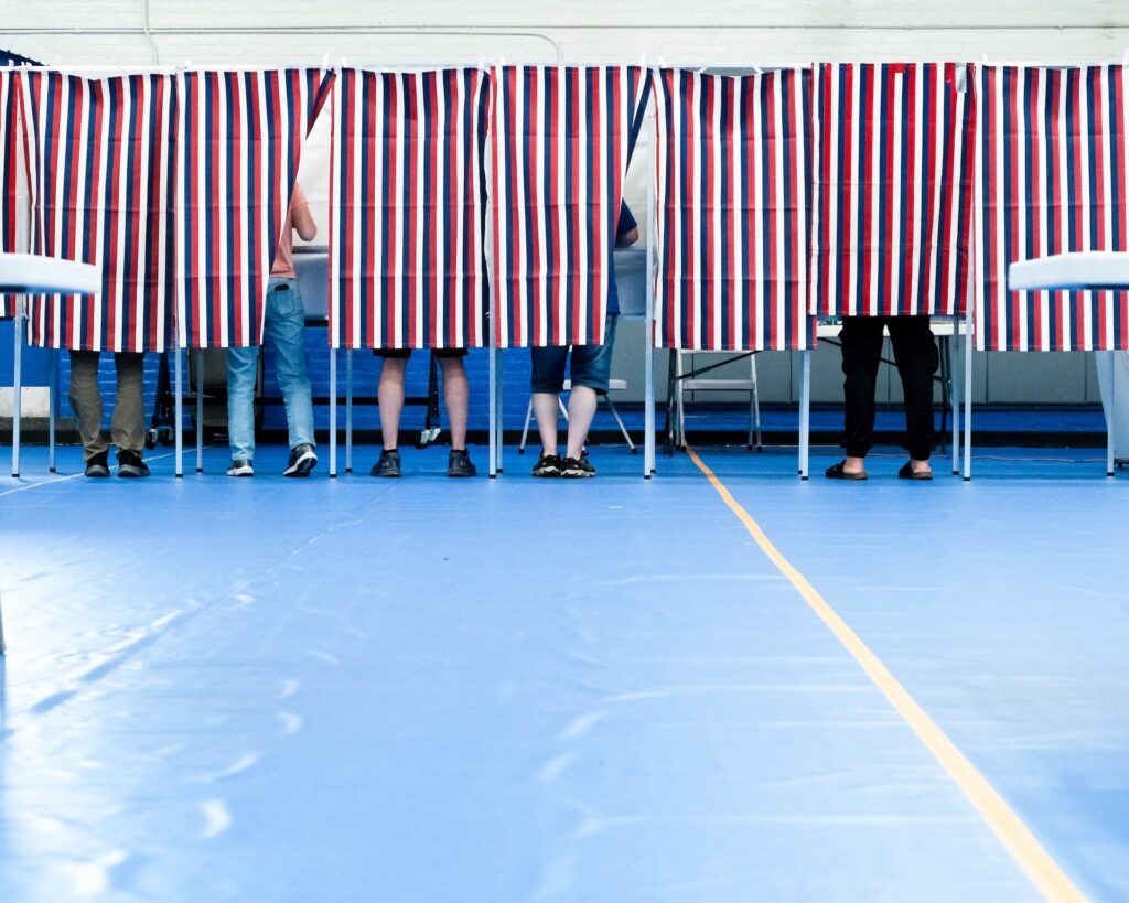 Voters standing behind striped privacy curtains in a polling place during an election. — Trump voter roll data lawsuit