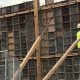Construction worker in a bright yellow shirt working on a wooden framework at a constructi — skilled trade worker shortage