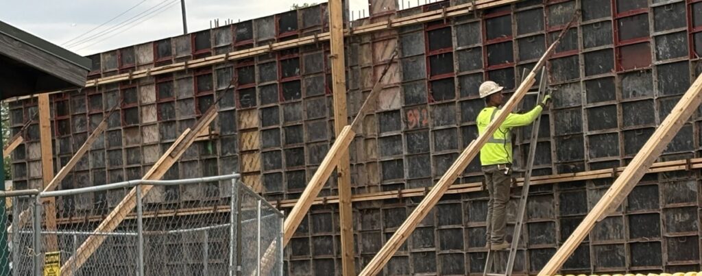 Construction worker in a bright yellow shirt working on a wooden framework at a constructi — skilled trade worker shortage